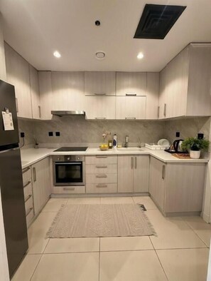 Une cuisine moderne avec des meubles en bois clair, des appareils électroménagers en acier inoxydable et un sol carrelé.