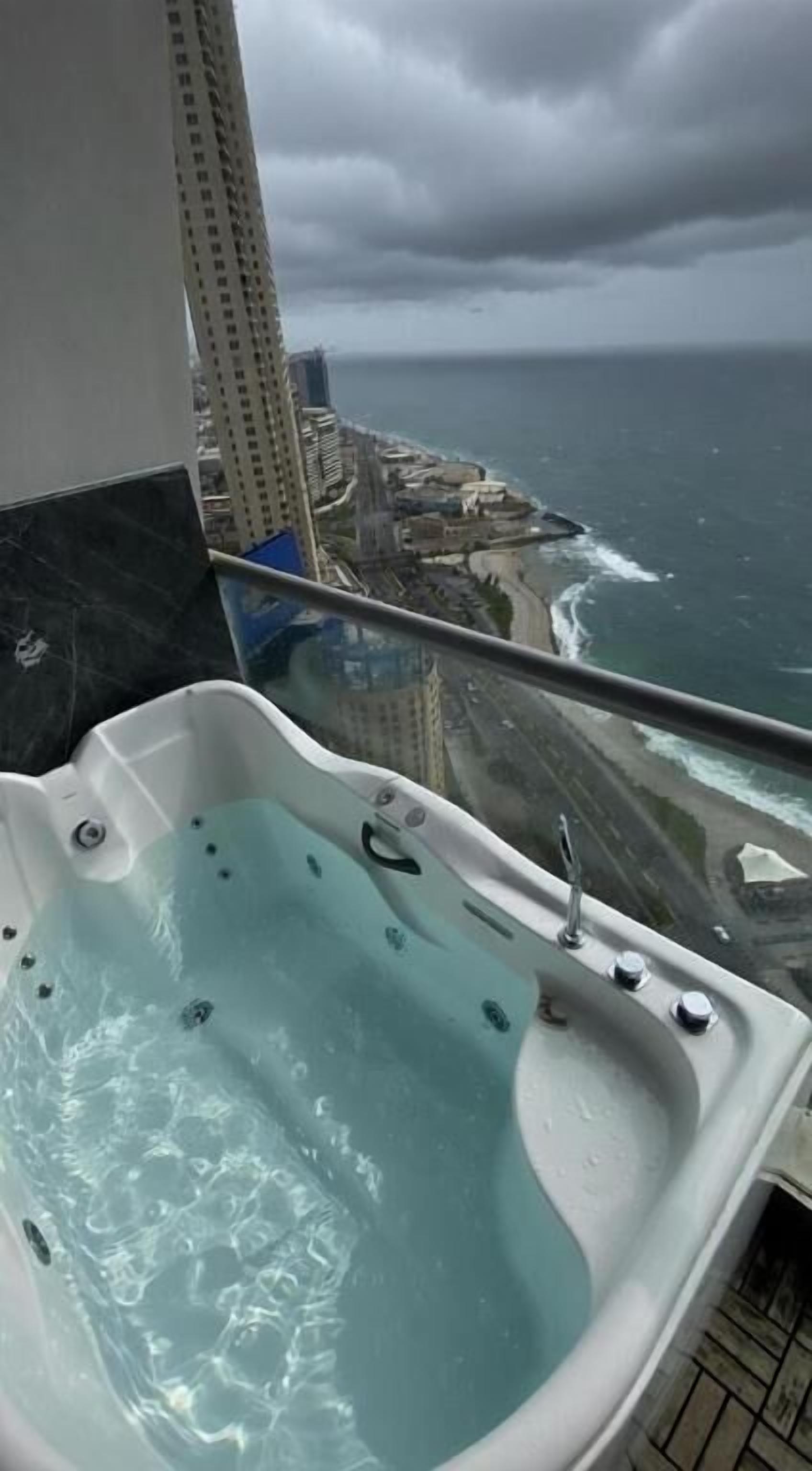 A hot tub on a balcony with a view of the ocean and a cityscape.