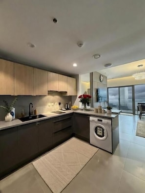 Una cocina moderna con armarios oscuros, lavadora integrada y un amplio ventanal con vistas.