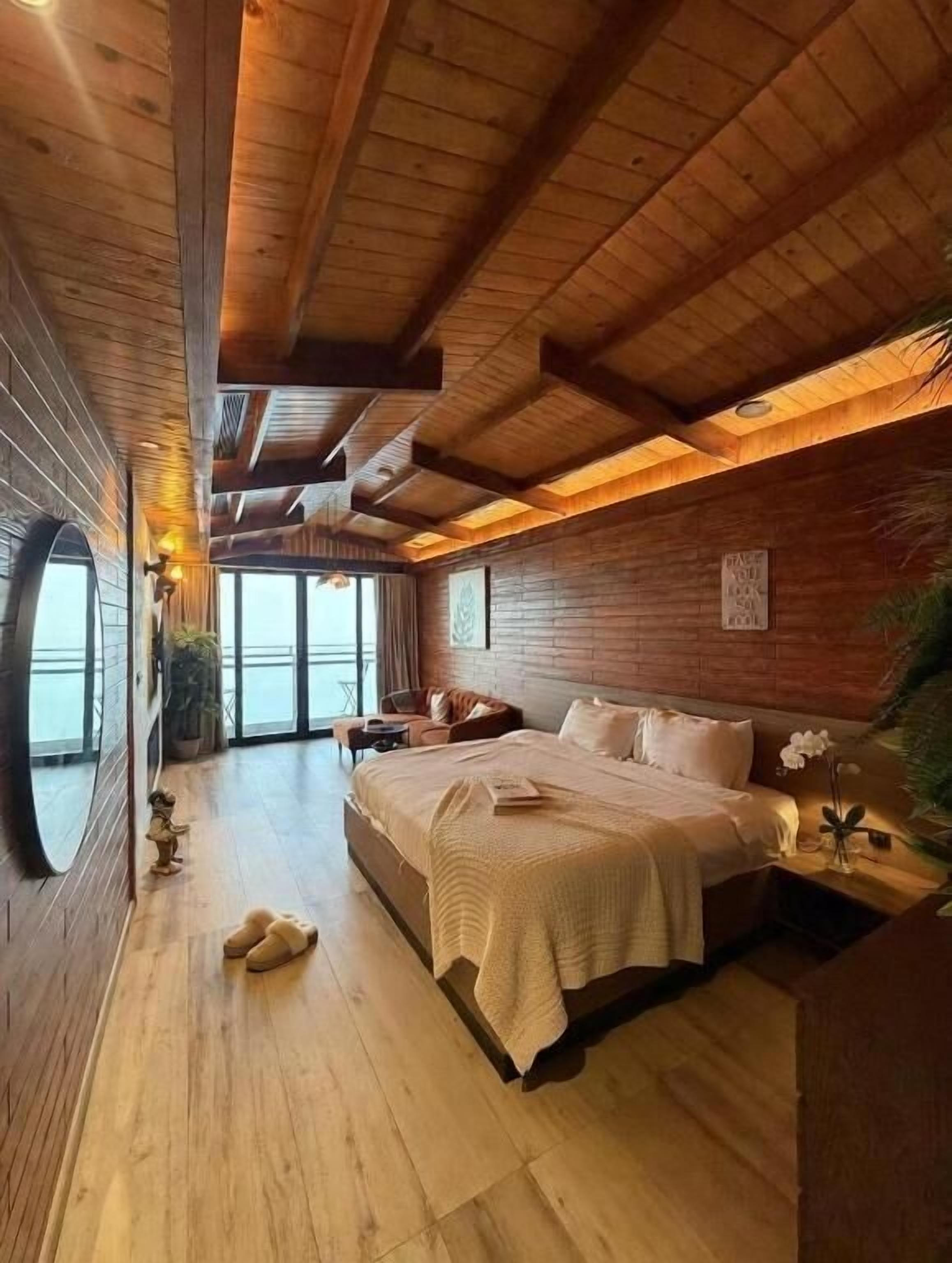 A wooden-paneled bedroom with a bed, bedside table, and a view through a window.