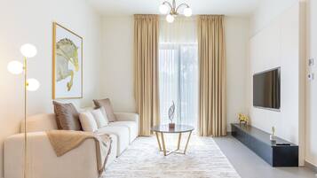 Un salon moderne comprenant un canapé, une table basse, un lampadaire, un téléviseur et une grande fenêtre avec des rideaux.