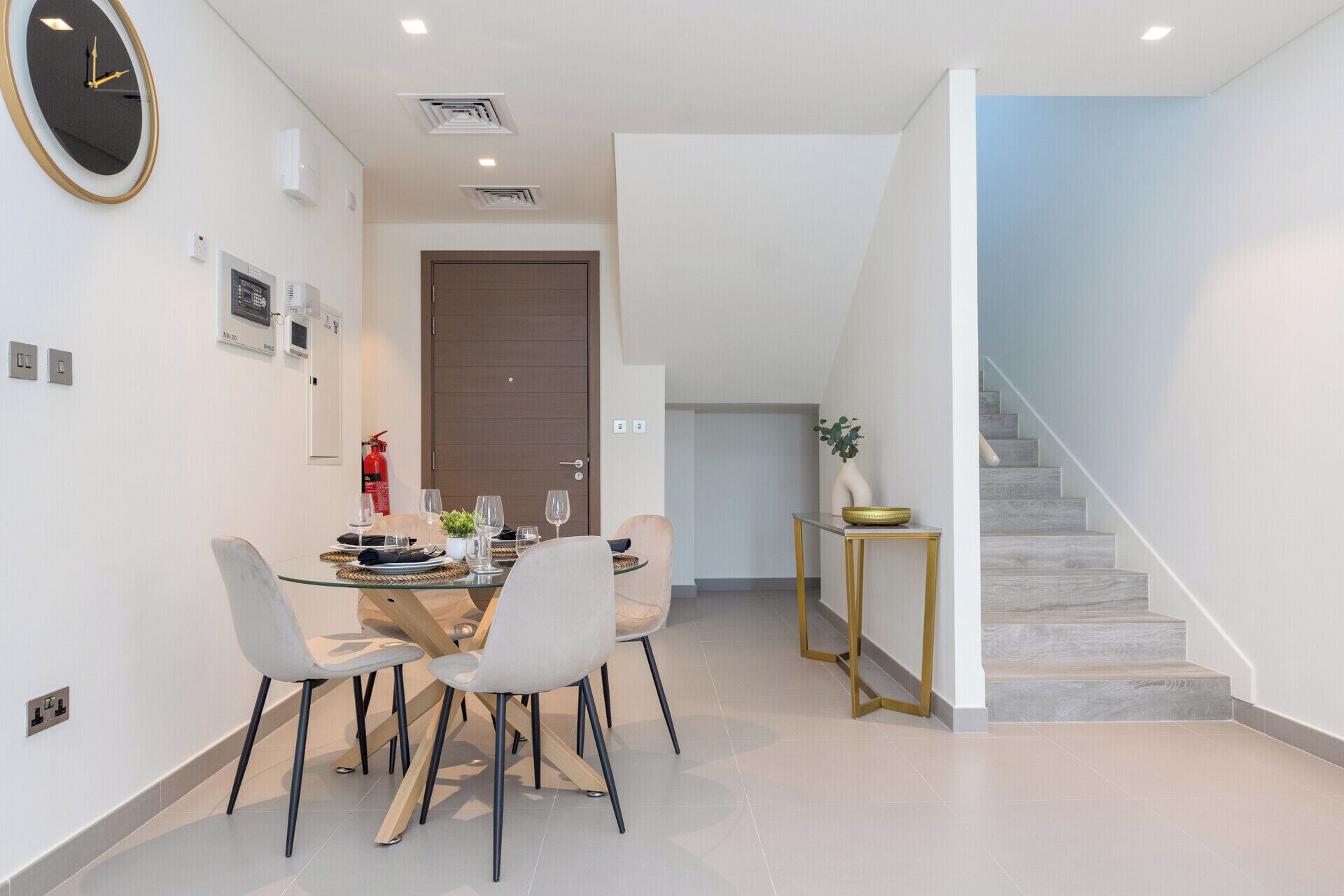 A modern dining area with a glass table, white chairs, and a clock on the wall.