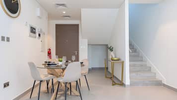 A modern dining area with a glass table, white chairs, and a clock on the wall.