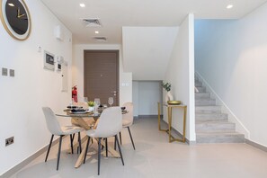 A modern dining area with a glass table, white chairs, and a clock on the wall. - Bloomfields 2BRplus Maid in Noya Viva  (Abu Dhabi)