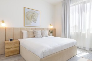 A bedroom with a bed, bedside tables, a wall-mounted light, a window with sheer curtains, and a framed artwork above the bed. - Bloomfields 2BR+M in Noya Viva-Yas (Abu Dhabi)