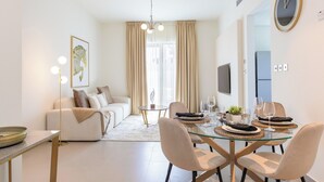 A modern living room with a sofa, a dining table set for two, and a large window with curtains. - Bloomfields 2BRplus Maid in Noya Viva  (Abu Dhabi)