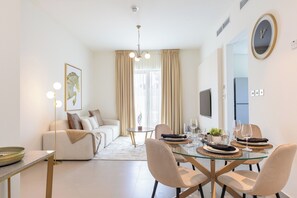 Ein modernes Wohnzimmer mit einer Couch, einem Esstisch für zwei Personen und einem großen Fenster mit Vorhängen.