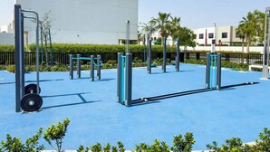 An outdoor gym with exercise equipment, a blue rubber floor, and a white building in the background. - Bloomfields 2BRplus Maid in Noya Viva  (Abu Dhabi)