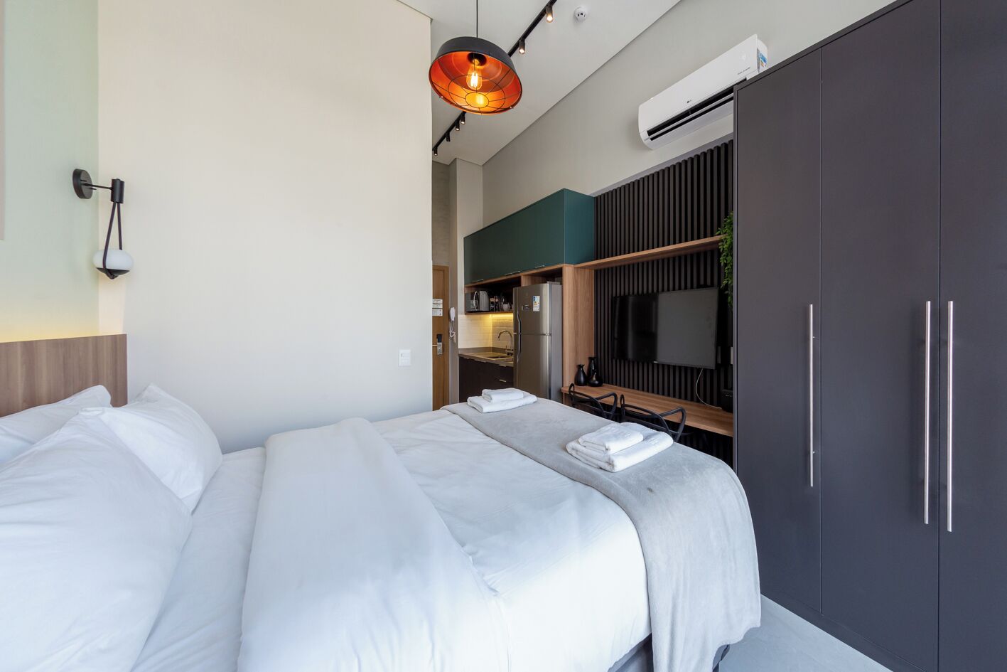 Et moderne hotelværelse med en stor seng, fjernsyn, skab og tekøkken.