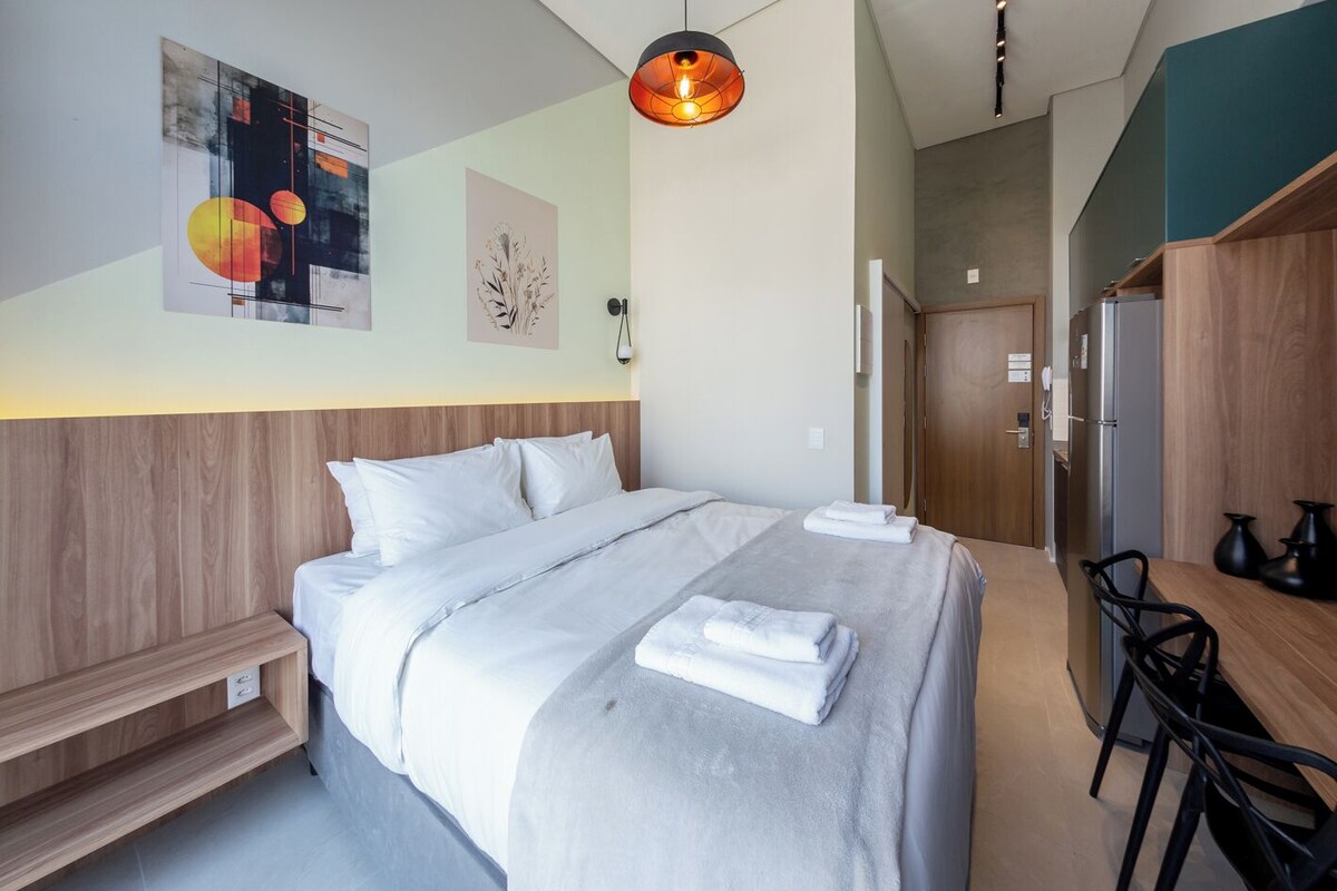 Ein modernes Hotelzimmer mit einem großen Bett, einer Bank, einem Schreibtisch mit Stühlen und Kunstwerken an den Wänden.