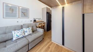 Un espace de vie moderne avec un canapé gris, un coin repas doté d’un réfrigérateur noir et des œuvres d’art encadrées accrochées au mur.