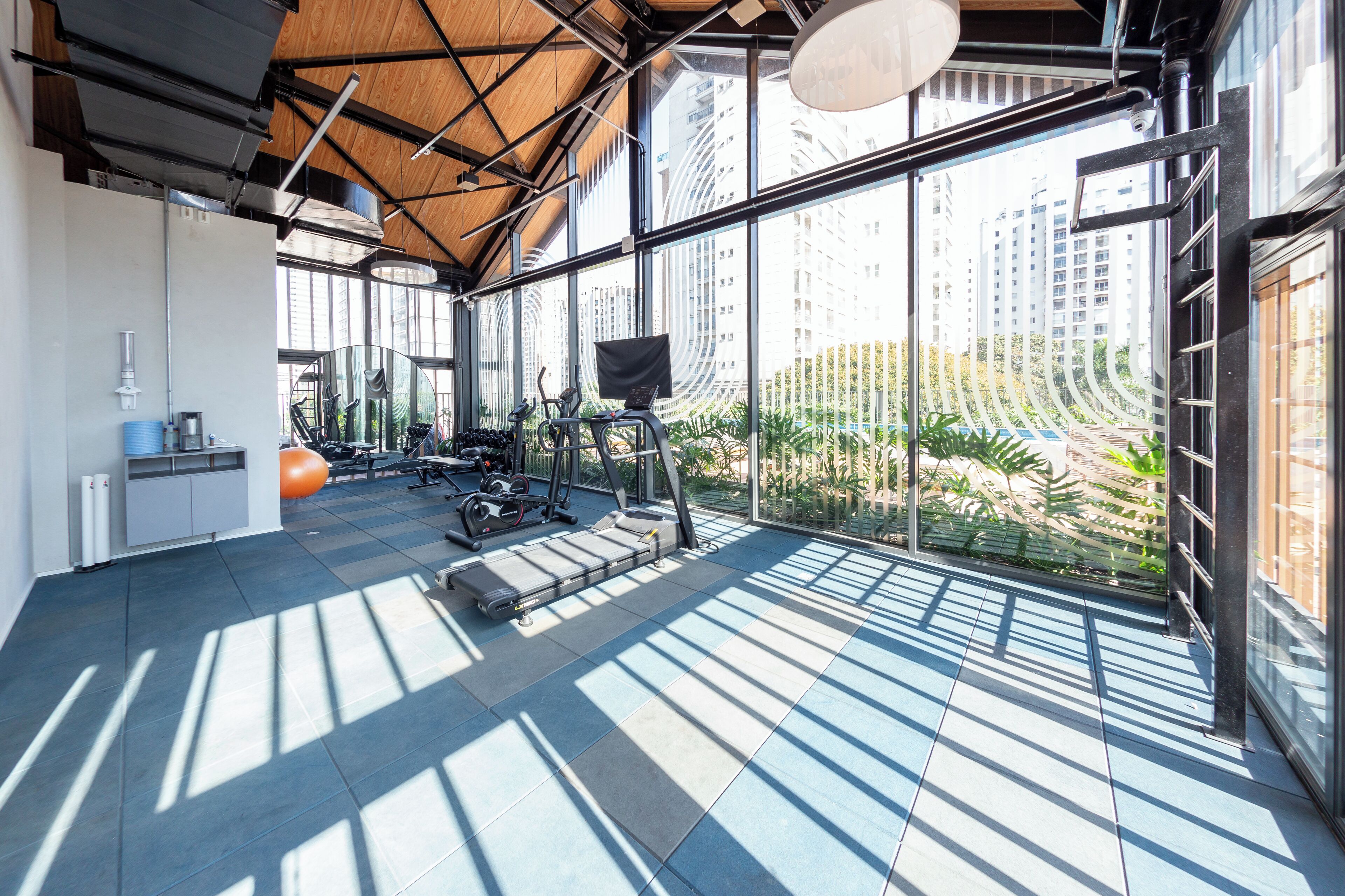 A gym with exercise equipment, large windows, and a view of tall buildings.