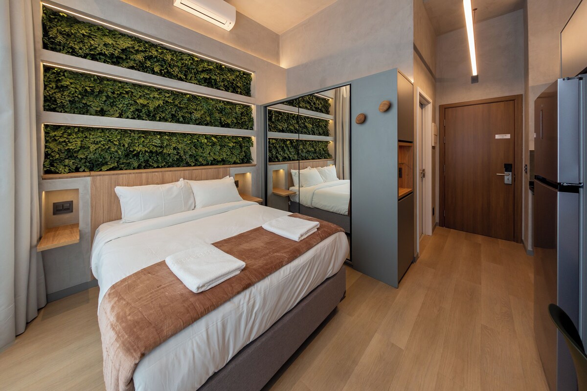 Ein modernes Hotelzimmer mit einem großen Bett, einem Spiegel, einer integrierten Grünwand und einer Holztür.