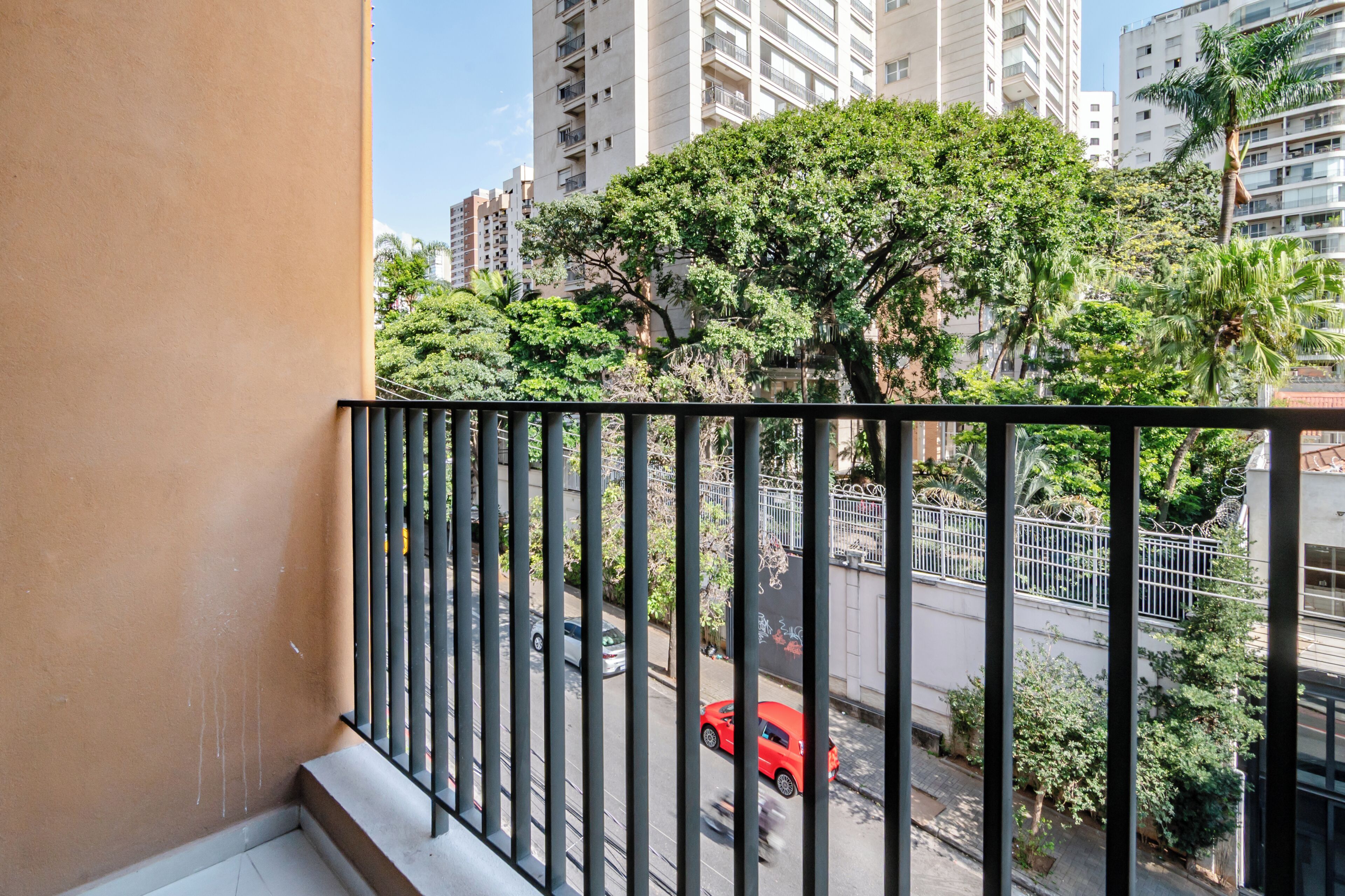 A balcony with a metal railing overlooking a street with cars and trees.