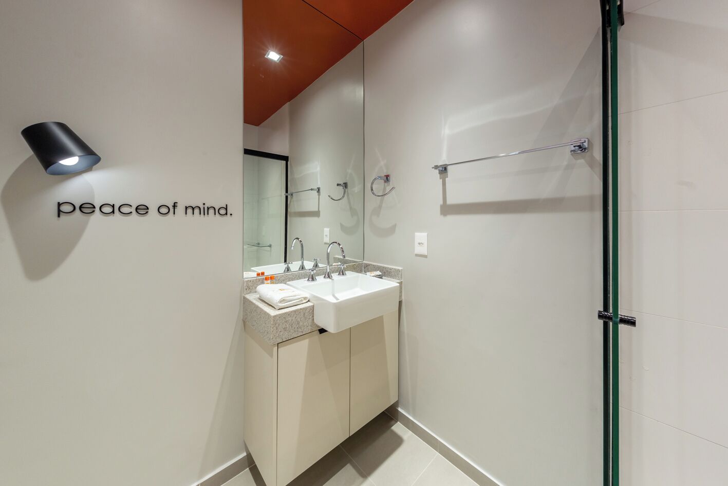 A modern bathroom with a white sink, two faucets, a mirror, and a glass shower enclosure.