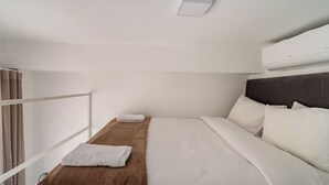Un lit simple avec une literie blanche, un plaid marron et une tête de lit.