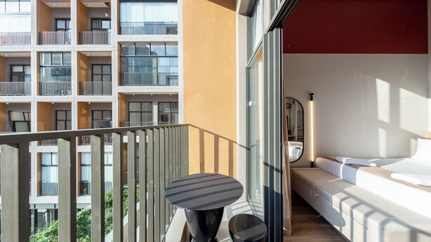 A balcony with a table and chairs, a sofa, and a bed in a modern apartment building.