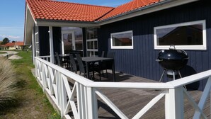 A covered outdoor area with a table and chairs, a barbecue grill, and a deck railing. - Beaside Wellness-chalet fur 10 Personen (Grossenbrode)