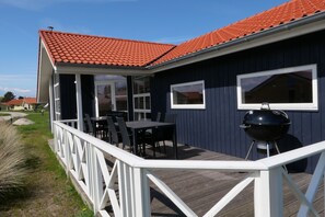 Ein überdachter Außenbereich mit Tisch und Stühlen, einem Grill und einem Decksgeländer.