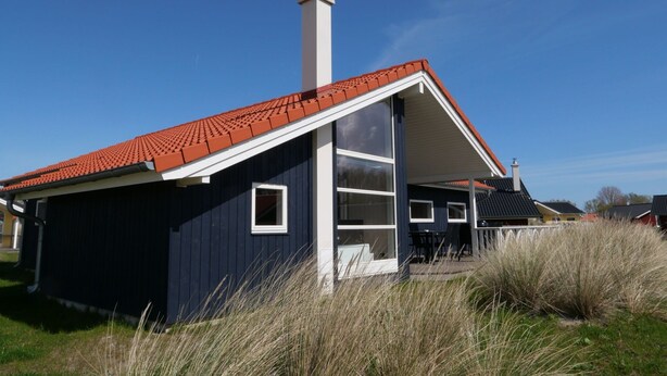 A house with a red-tiled roof, a chimney, and a large window. - Beaside Wellness-chalet fur 10 Personen (Grossenbrode)