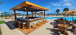 A poolside bar area with a stone counter, wooden stools, and a pergola overhead.