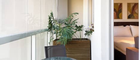 A balcony with a glass table, chairs, and potted plants.