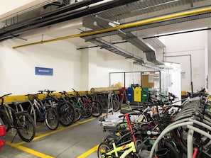 Ein Fahrradstellplatz mit mehreren Fahrrädern, einem Schild, das ihn als Fahrradstation kennzeichnet, und darüberliegenden Rohren.