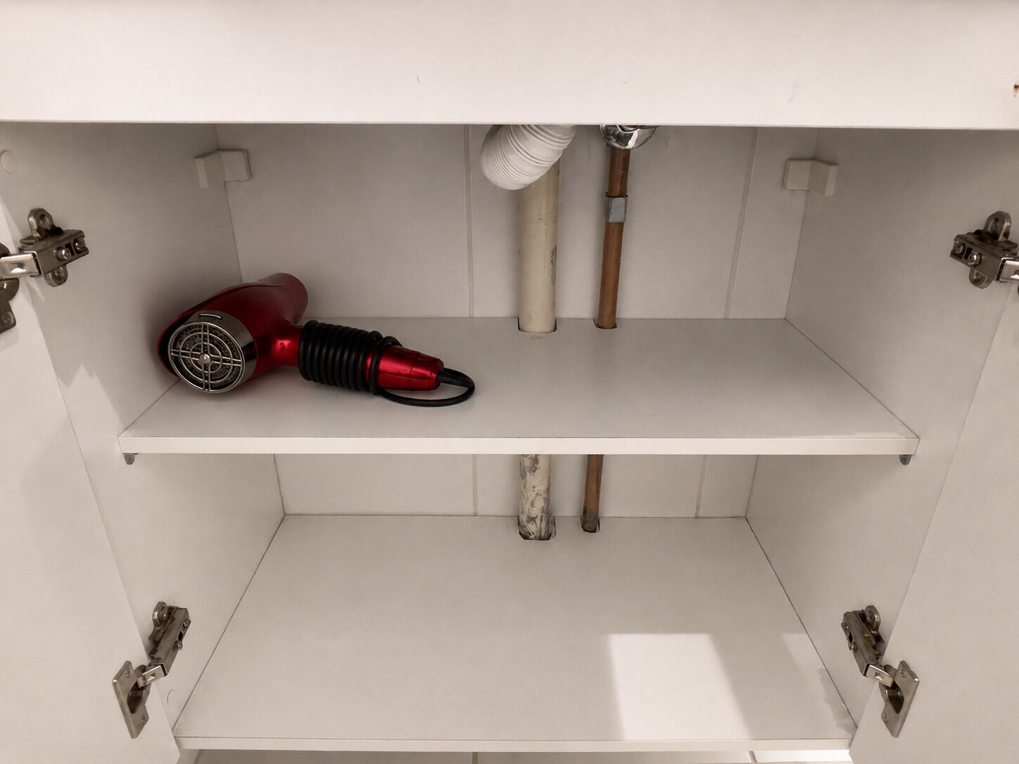 A white cabinet with a red hairdryer and a white brush.