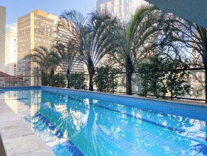 A swimming pool with clear blue water, surrounded by trees and buildings. - Ampm Paulicéia Centro (São Paulo)