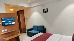 A hotel room with a bed, a TV mounted on a wooden cabinet, a blue sofa, and a door leading to another room.