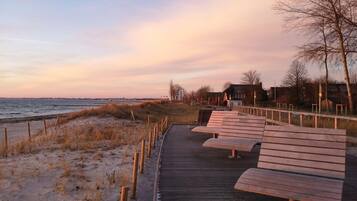 A wooden boardwalk leading to a beach with benches and a fence.