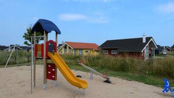 A playground with a slide and swings, surrounded by houses and a clear sky.