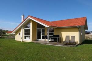 A yellow building with a red-tiled roof, a covered patio with a table and chairs, and a large sliding glass door.