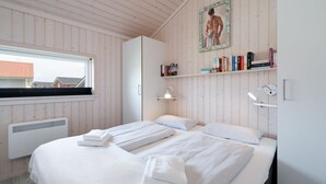 A bedroom with two beds, a window, a radiator, a bookshelf, and a painting on the wall. - Urlaub in der Baltischen Natur fur 6 Personen (Grossenbrode)