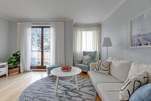A living room with a sofa, a round coffee table, a chair, a lamp, and a large window with curtains. - Amalfi - Quiet Family Stay Sopot (Sopot)