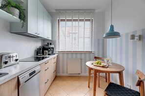 Eine moderne Küche mit integriertem Toaster, Wasserkocher und Kaffeemaschine, einem Esstisch mit Stuhl sowie einem Fenster mit Jalousien.