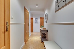 Ein Korridor mit einer Holztür, einem kleinen Tisch mit einer Vase und einem Korb, sowie einem an der Wand befestigten Spiegel.