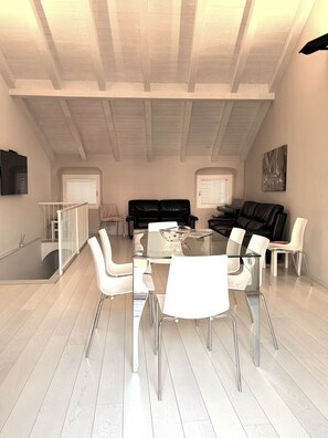 A spacious living area with a high ceiling, a glass-top dining table surrounded by chairs, and a black leather sofa. - Budello di Alassio, spacious apartment 30 meters from the beach, garage included (Alassio)