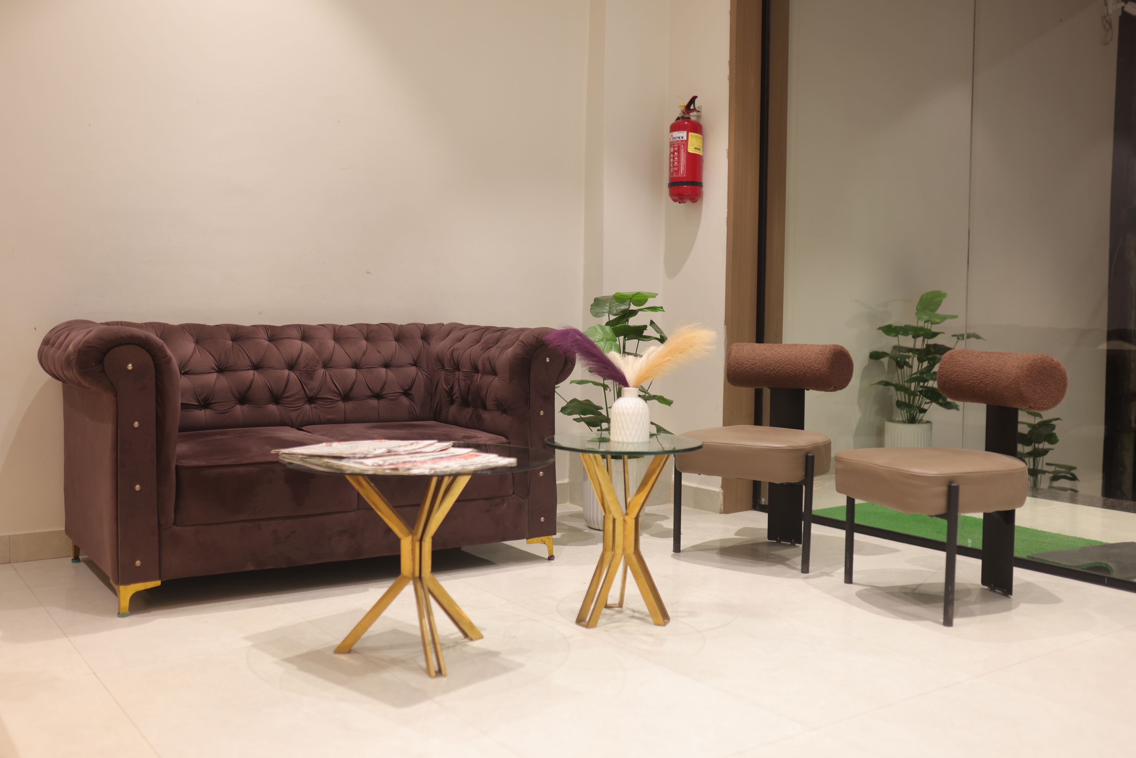 Una sala de estar moderna con un sofá marrón, una mesa de vidrio con patas doradas y una pequeña maceta blanca con una planta.