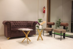 A modern living room with a brown sofa, a glass table with gold legs, and a small white vase with a plant.