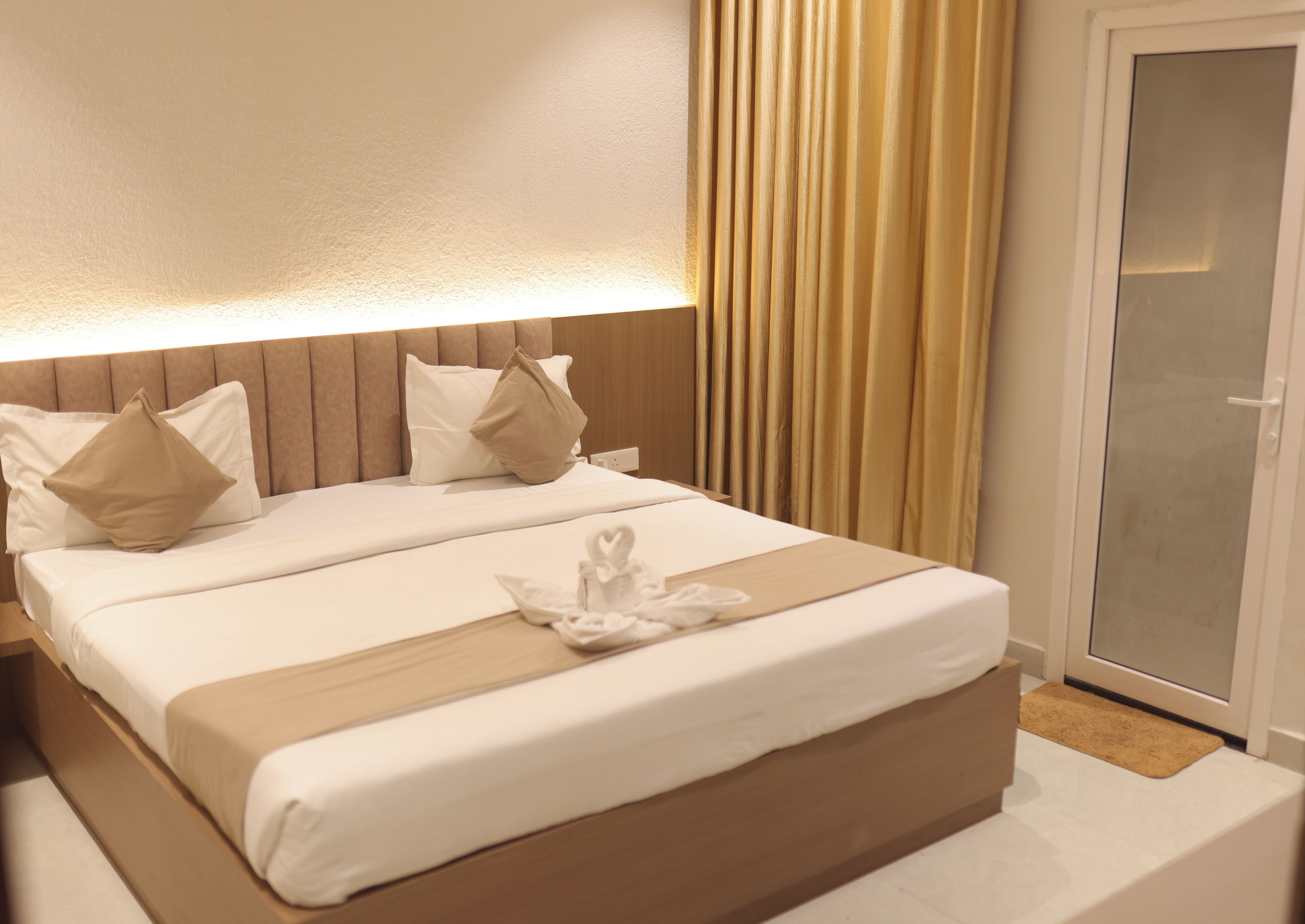 A hotel room with a bed, pillows, a bedside table, and a sliding glass door.