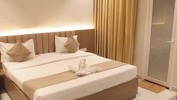 A hotel room with a bed, pillows, a bedside table, and a sliding glass door.