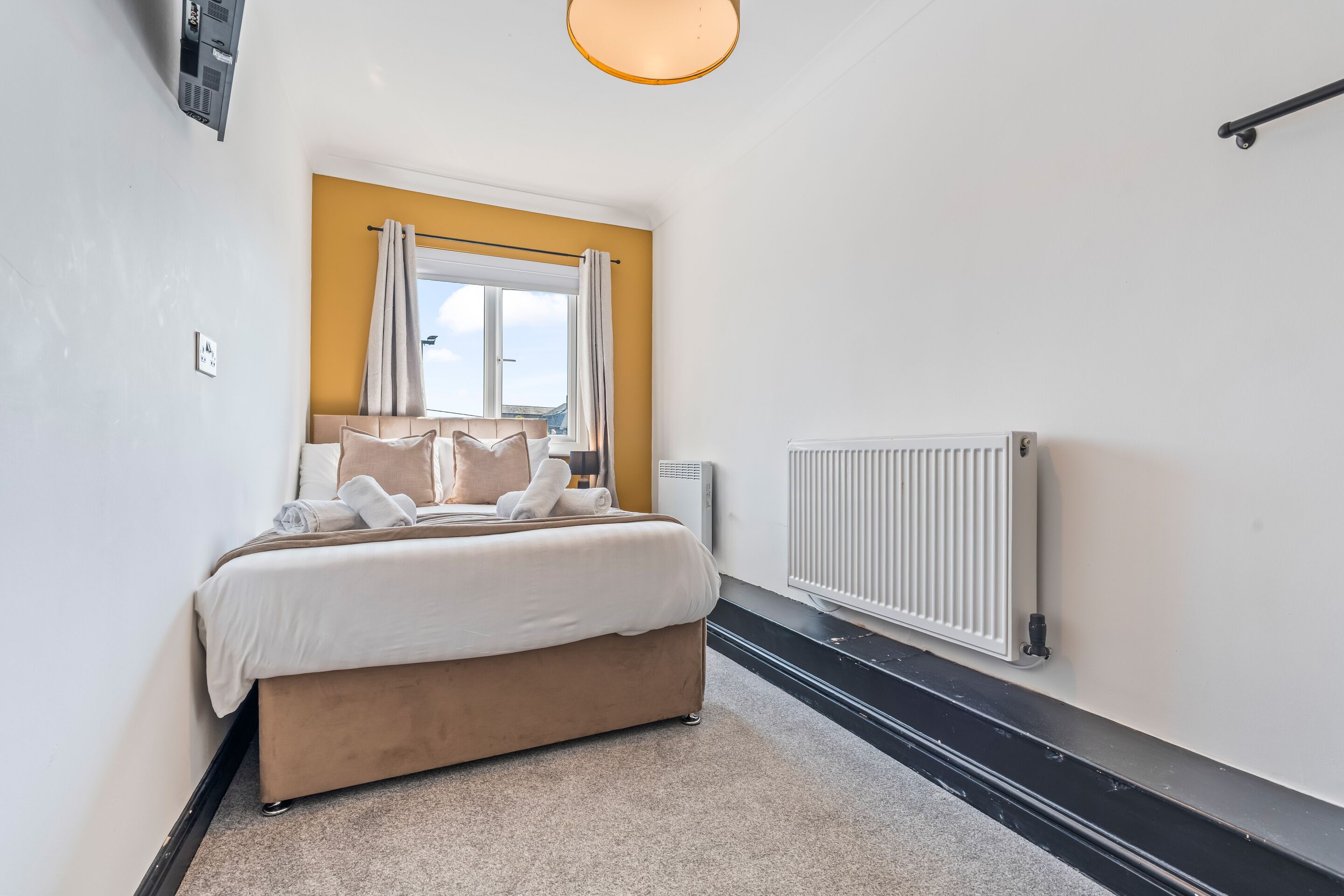 A bedroom with a bed, a radiator, and a window with curtains.