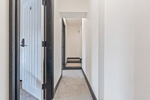 Un pasillo con una puerta a la izquierda, un interruptor de luz en la pared y suelo cubierto de alfombra.