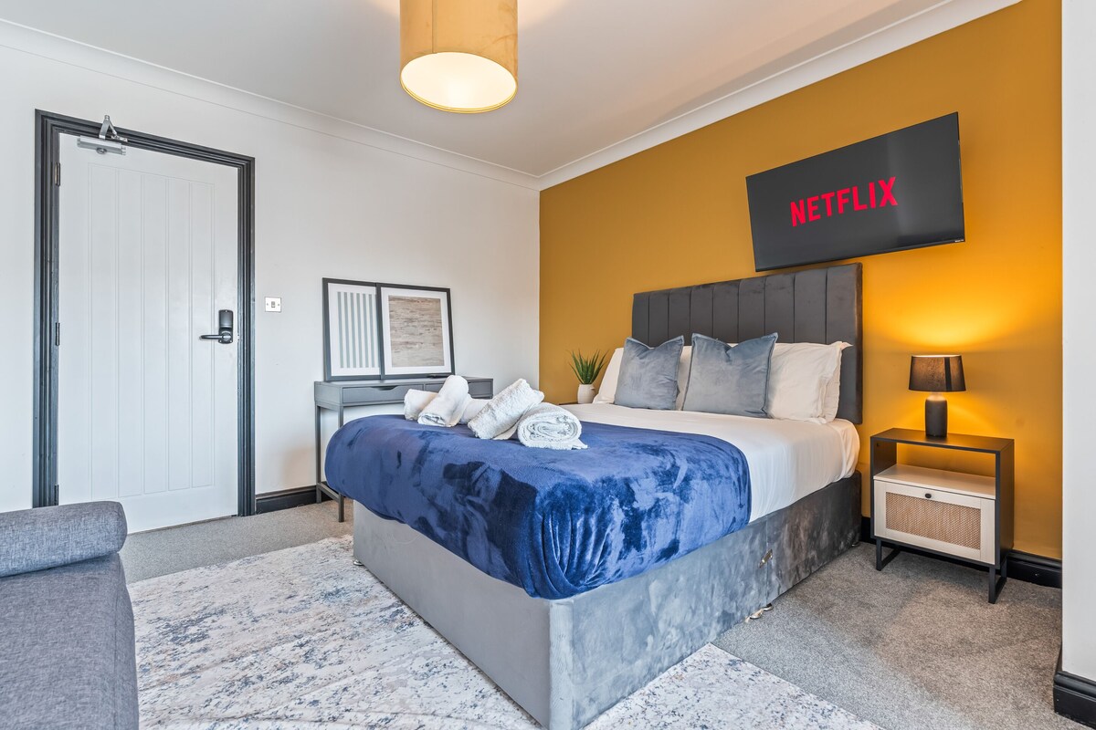 Un dormitorio moderno con cama, mesita de noche, televisor en la pared y una puerta.