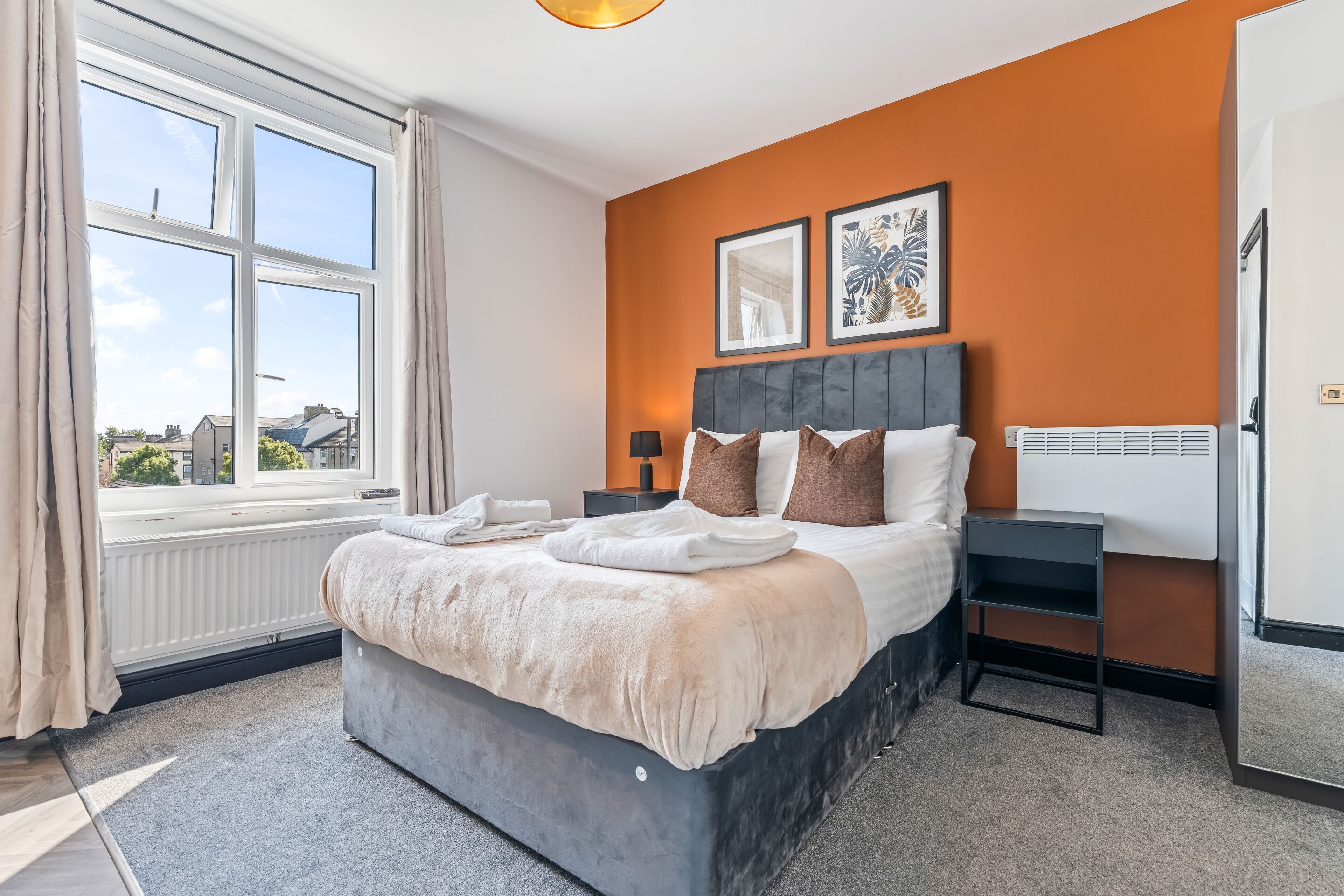 A hotel room with a large bed, a window with curtains, a radiator, and two framed pictures on the wall.