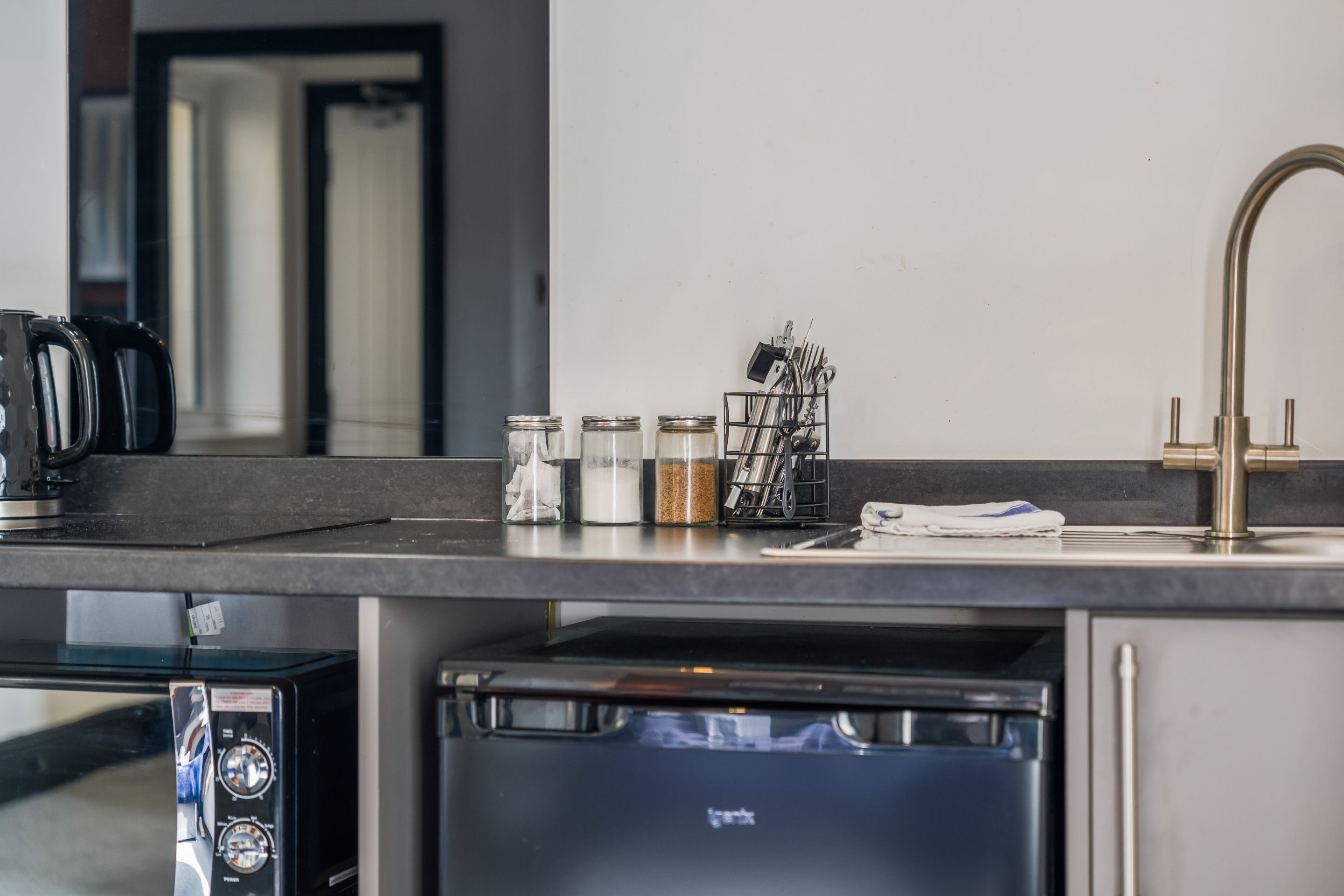 A kitchen counter with a coffee maker, jars of spices, and a dish rack with utensils.