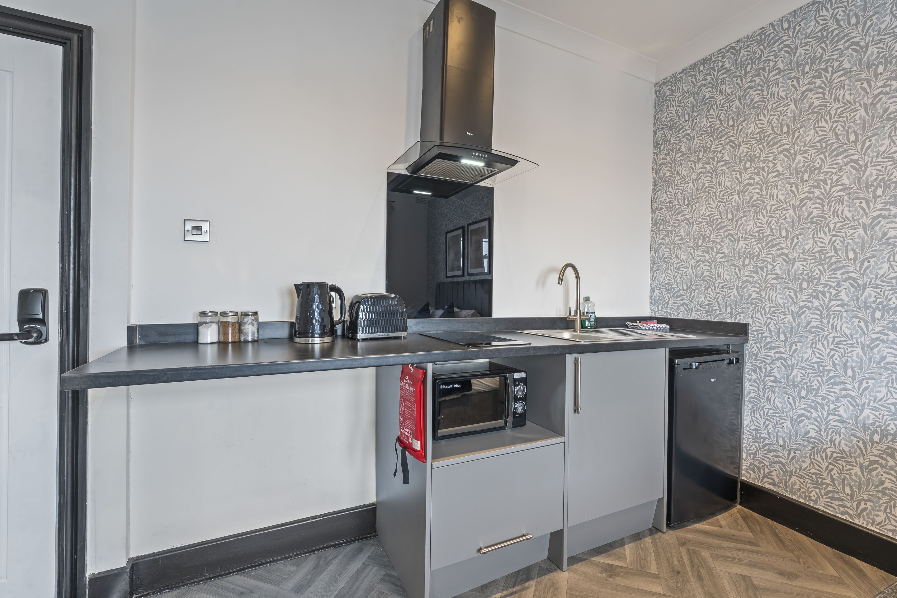 A compact kitchen with a built-in oven, a coffee maker, and a kettle.