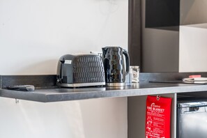 Una encimera de cocina con un hervidor, una taza y un cartel de manta ignífuga.
