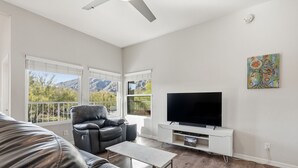 A living room with a leather sofa, a recliner, a coffee table, a flat-screen TV on a white stand, and a painting on the wall. - Mountain, Canyon & Golf Course Views from all Windows in this corner 3 bedrm (Tucson)